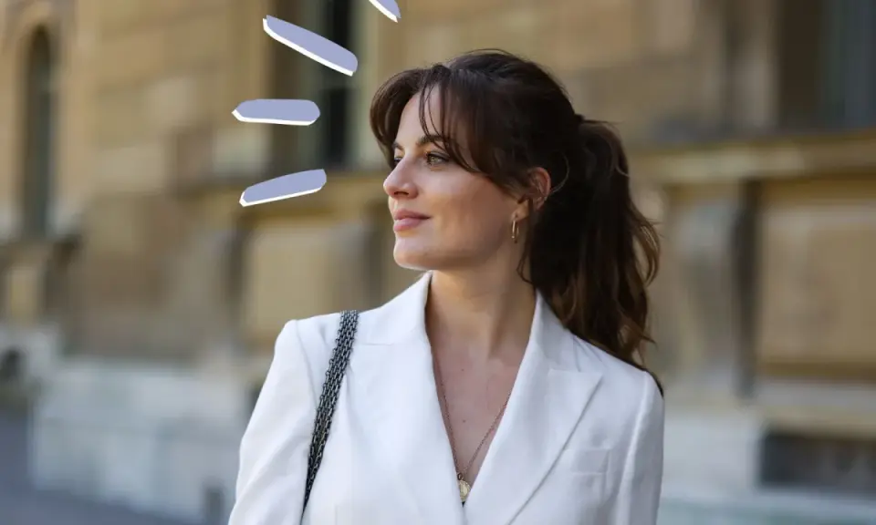 Frauen mit Curtain Bangs stylen ihre Haare lässig zu einem Pferdeschwanz. Der weiße Blazer unterstreicht den eleganten Look.