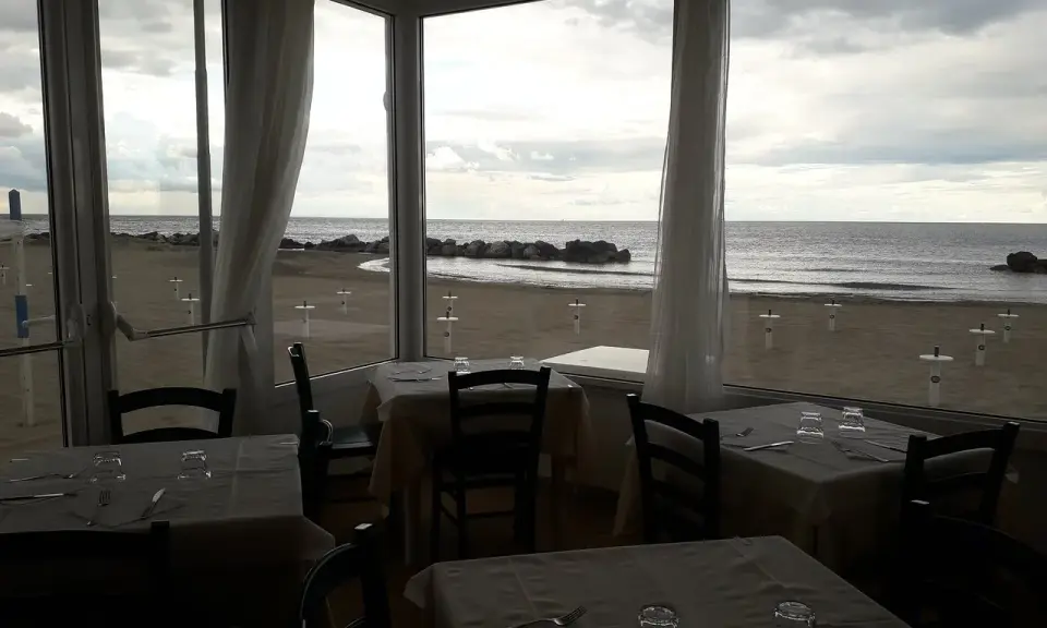 Tavoli apparecchiati in un ristorante con vista sulla spiaggia di Misano durante la bassa marea.