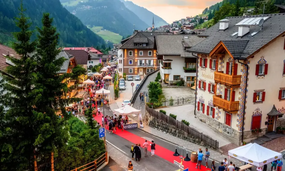 Festa a Santa Cristina Val Gardena con gente, bancarelle e un tappeto rosso.