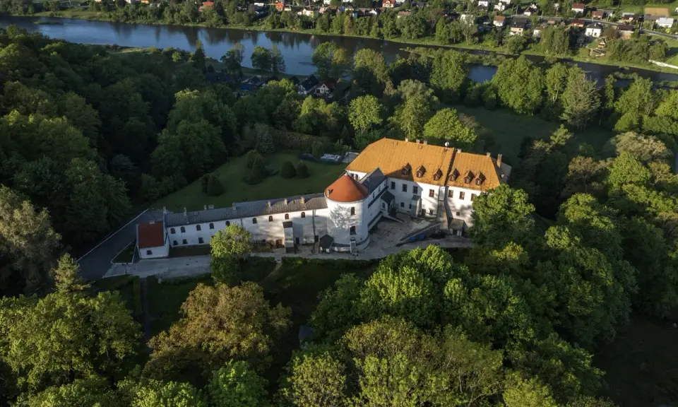 Zamek w Lesku otoczony zielenią, z widokiem na rzekę i miasteczko.