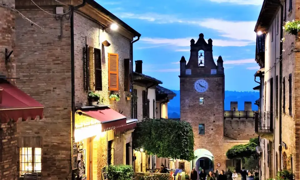 Borgo medievale illuminato al crepuscolo, con torre dell'orologio e vicoli suggestivi. Perfetto per scoprire cosa vedere vicino a Gradara.
