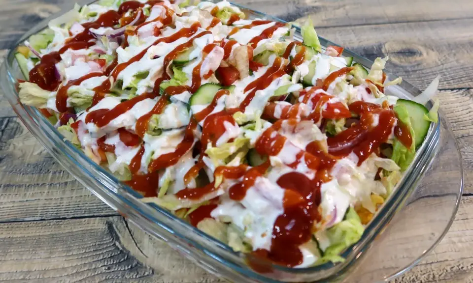 Kapsalon z kurczakiem, sałatą, pomidorami, ogórkiem i sosami w szklanej misce.