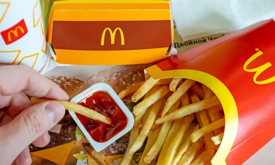 Ręka zanurza frytkę w keczupie. Obok pudełko z frytkami i burgerem. McDouble kcal to smak, który znasz.