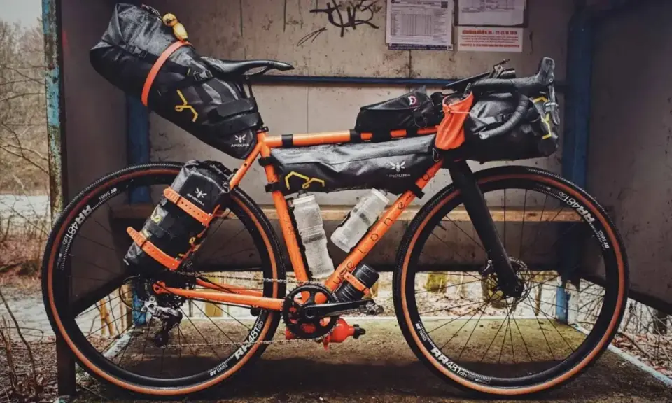 Orange Rennrad mit Bikepacking-Taschen, bereit für Abenteuer.