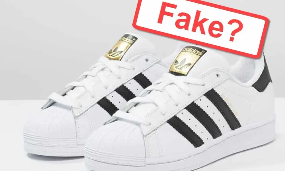 Weiße Adidas Sneaker mit schwarzen Streifen und goldenem Logo. Ein rotes Schild fragt: "Fake?". So kannst du Adidas Fake erkennen.