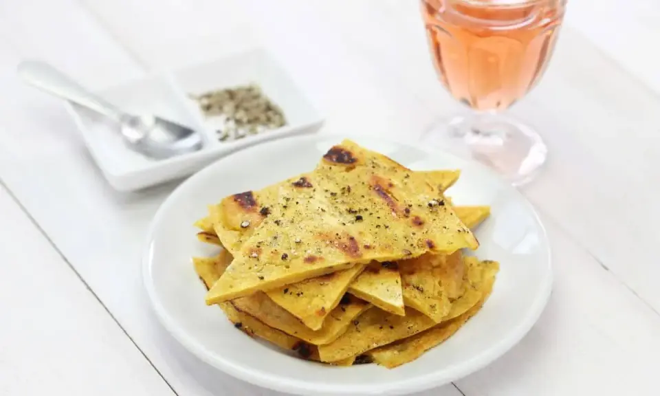 Une assiette de socca à la poêle, coupée en triangles et saupoudrée de poivre, à côté d'un verre de rosé.