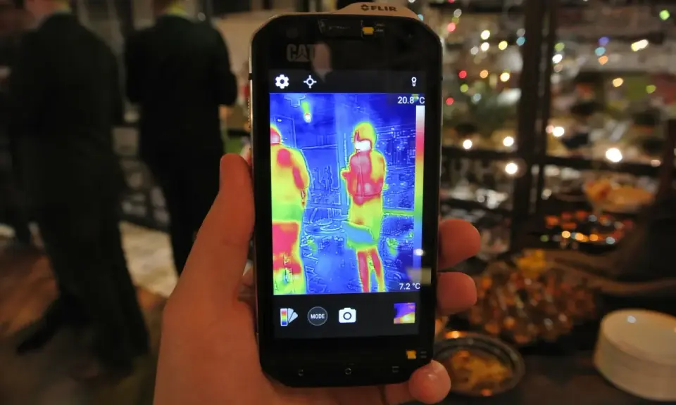 Ręka trzyma smartfon Cat S60 z włączoną termowizją, pokazującą dwie osoby w cieplejszych barwach.