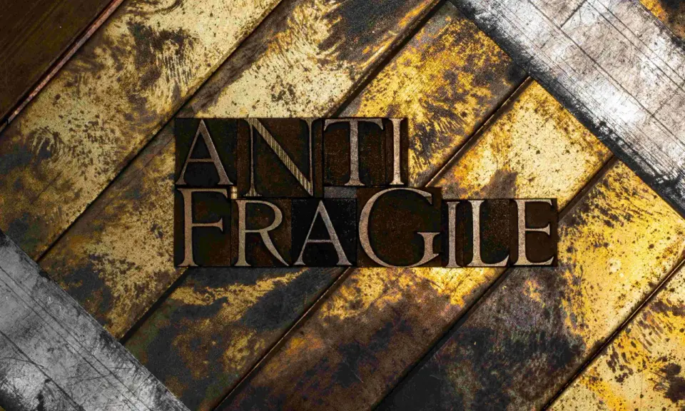 Lettere di metallo con la scritta "ANTI FRAGILE" su uno sfondo ruvido e dorato, simbolo di antifragilità e resilienza.