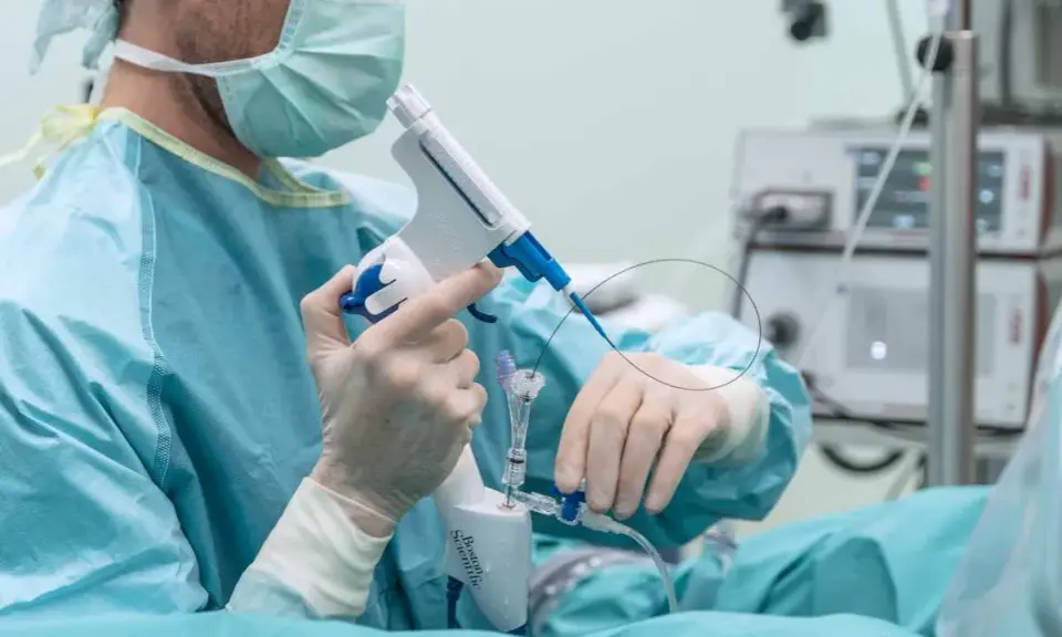 Chirurg w masce i rękawiczkach trzyma przyrząd medyczny do biopsji.