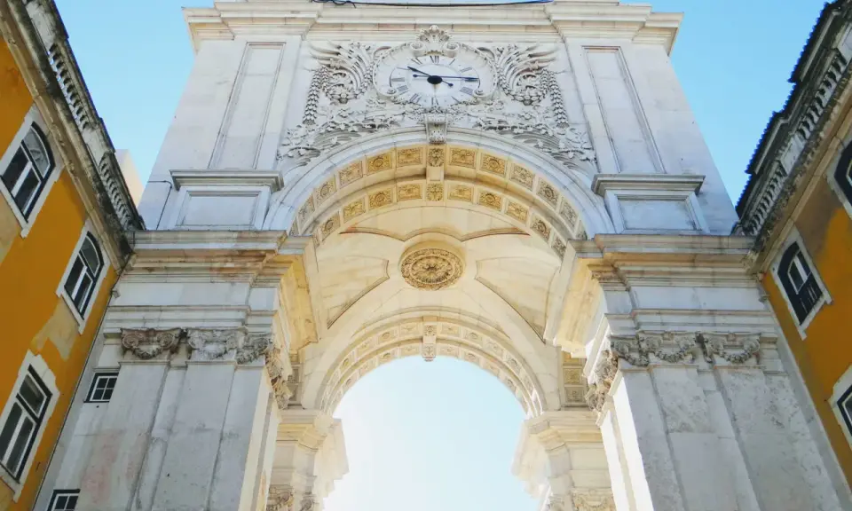 Der Arco da Rua Augusta in Lissabon, ein imposanter Triumphbogen mit einer Uhr und kunstvollen Verzierungen, ragt majestätisch in den blauen Himmel.