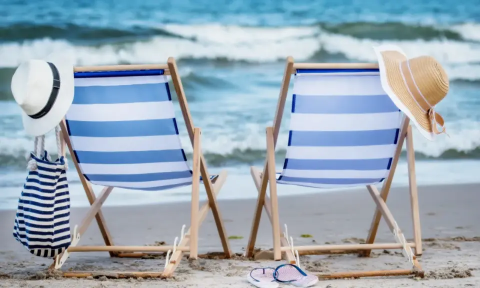 Dwa leżaki na plaży, gotowe na idealny weekend nad morzem. W tle szum fal i błękitne niebo.