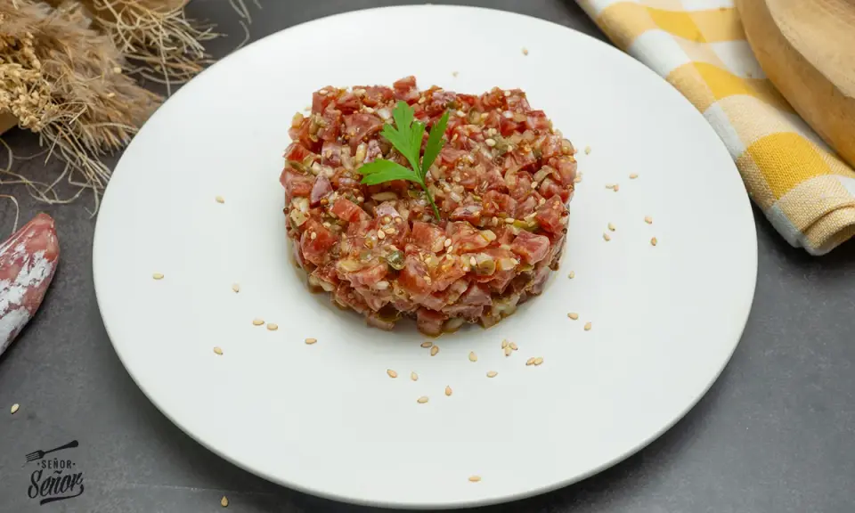 Delicioso steak tartar de fuet, picado finamente con especias y semillas de sésamo, adornado con una hoja de perejil.