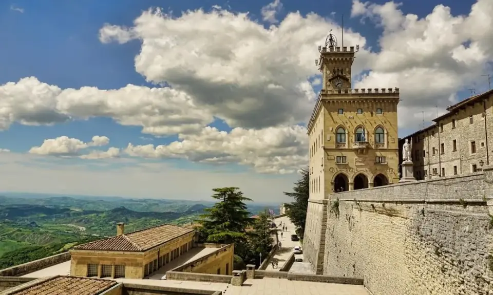 Torre del Campanone e Palazzo Pubblico nel **San Marino centro**, con vista panoramica sulle colline verdi sotto un cielo azzurro e nuvoloso.