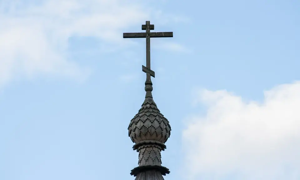 Drewniany krzyż na kopule cerkwi, symbol religii w Gruzji, na tle błękitnego nieba z chmurami.