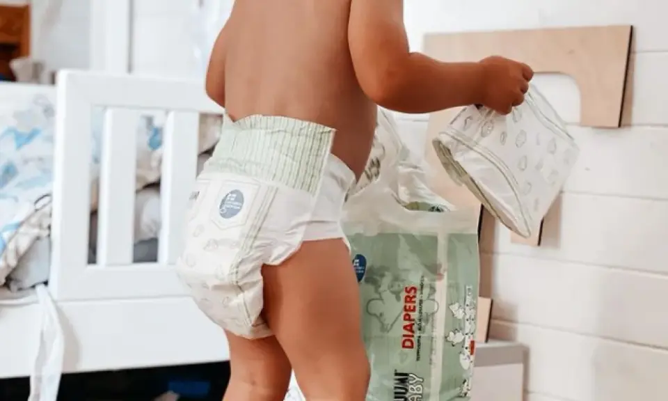 Un bimbo con un pannolino indosso, vicino a una confezione di pannolini. Sembra che i pannolini scadano, ma non c'è fretta.