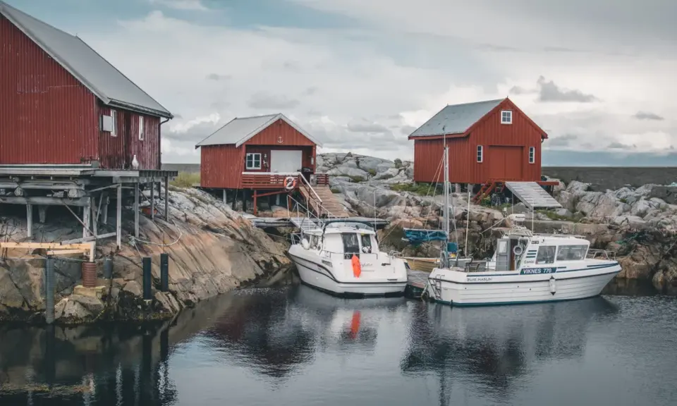 Norwegia: praca w norwegii dla par z zakwaterowaniem. Czerwone domki rybackie i łodzie przy skalistym brzegu.