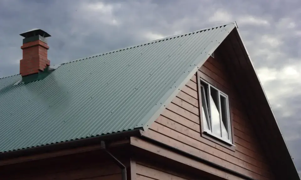 Dach domu pokryty zieloną blachą trapezową, z ceglanym kominem i drewnianą ścianą. Precyzyjne cięcie blachy trapezowej zapewnia estetykę.