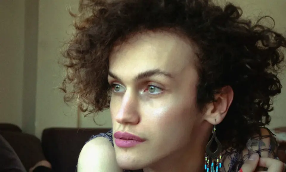 Portret osoby z kręconymi włosami, która zastanawia się nad przyczynami dysforii płciowej.