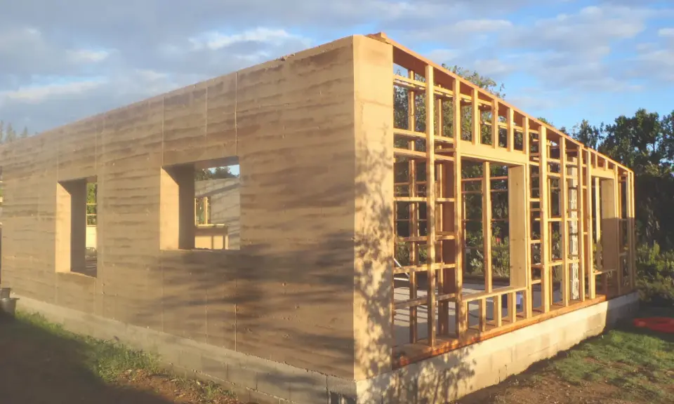 Construction d'une maison terre crue aux murs stratifiés, avec une ossature bois visible pour la suite.