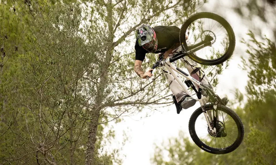 Tomas Lemoine fliegt mit seinem Mountainbike durch die Luft, umgeben von Bäumen.