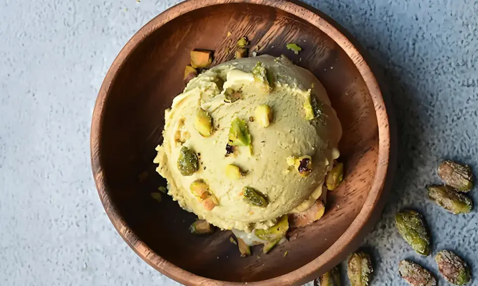 Cremoso helado de pistacho con trozos de pistacho en un cuenco de madera.