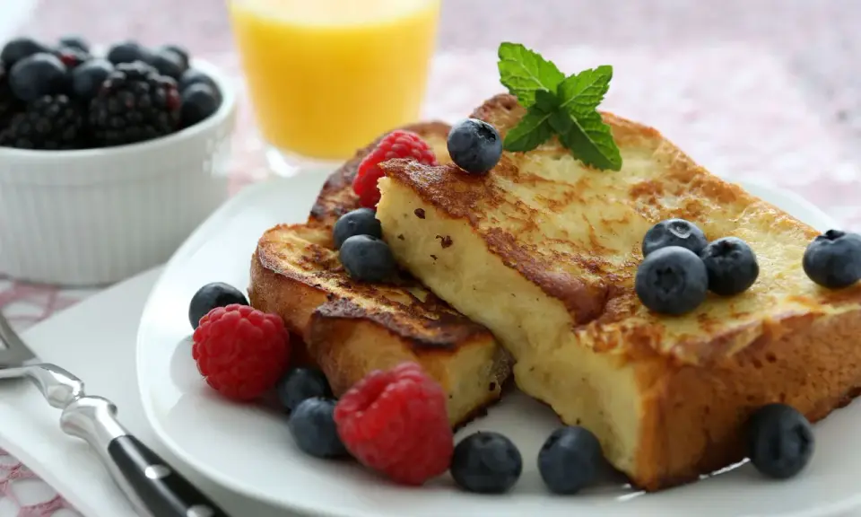 Deliciosa french toast receta, dorada y esponjosa, adornada con frambuesas, arándanos y menta. Un desayuno perfecto.