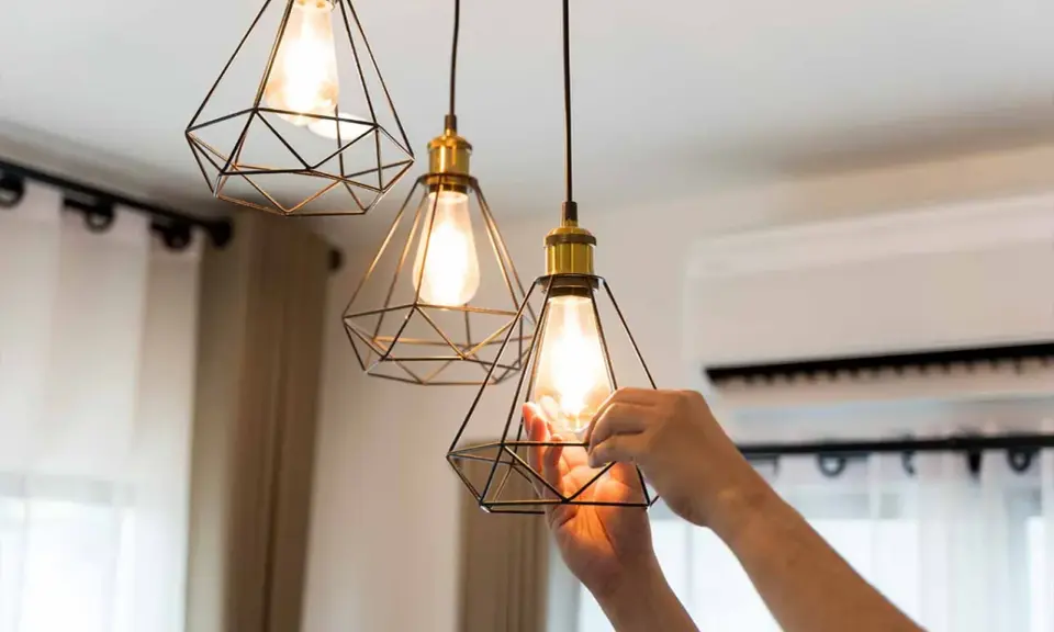 Man changing a lightbulb in a modern geometric pendant lamp, part of the simple home interiors.