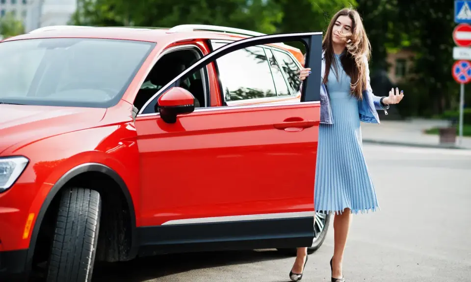 Mujer elegante sale de un monovolumen o SUV rojo brillante.