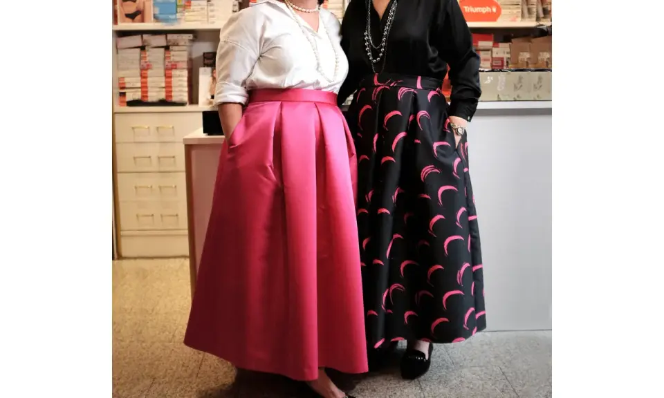 Due donne mostrano diversi tipi di gonne: una rosa a pieghe e una nera con stampa a mezzelune rosa.