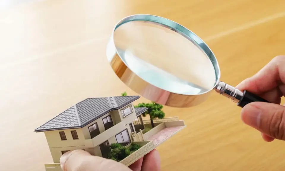 Main tenant examine un modèle de maison avec une loupe pour expertiser un tableau.