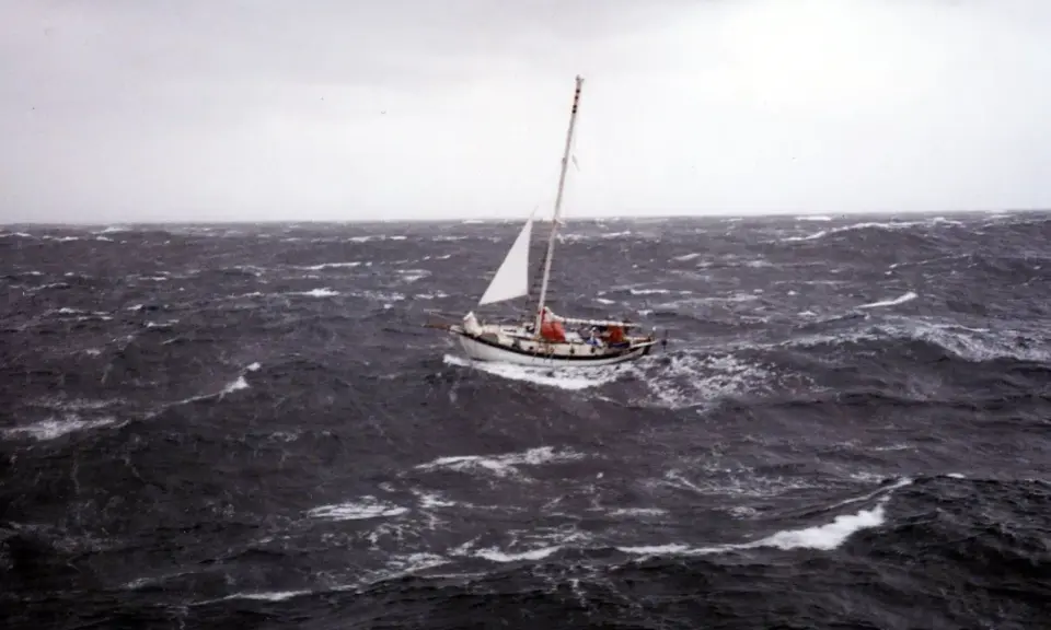 Un voilier affronte une mer agitée, sa voile blanche tendue. La mise à la cape est une manœuvre de survie face aux éléments déchaînés.