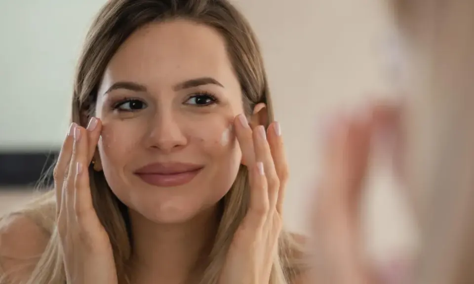 Une femme applique de la crème sur son visage, un geste pour enlever ride et garder une peau jeune.