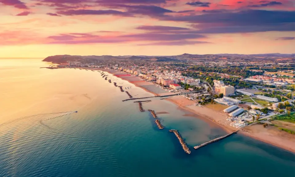 Alba rosata sul porto di Cattolica, con la costa e le spiagge dorate che si estendono verso l'orizzonte.