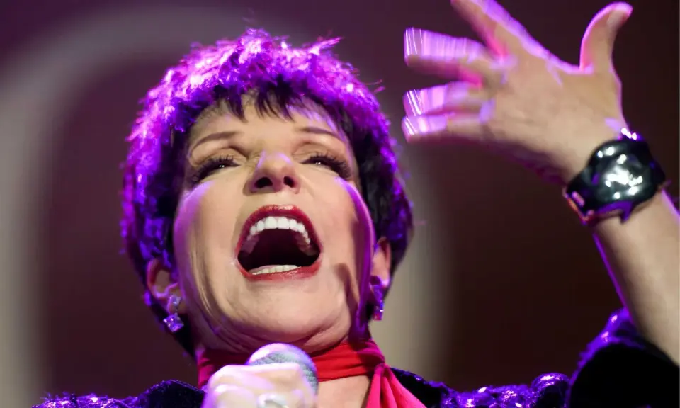 Liza Minnelli, en ikonisk artist, sjunger med passion på scenen, hennes ansikte upplyst av lila ljus.