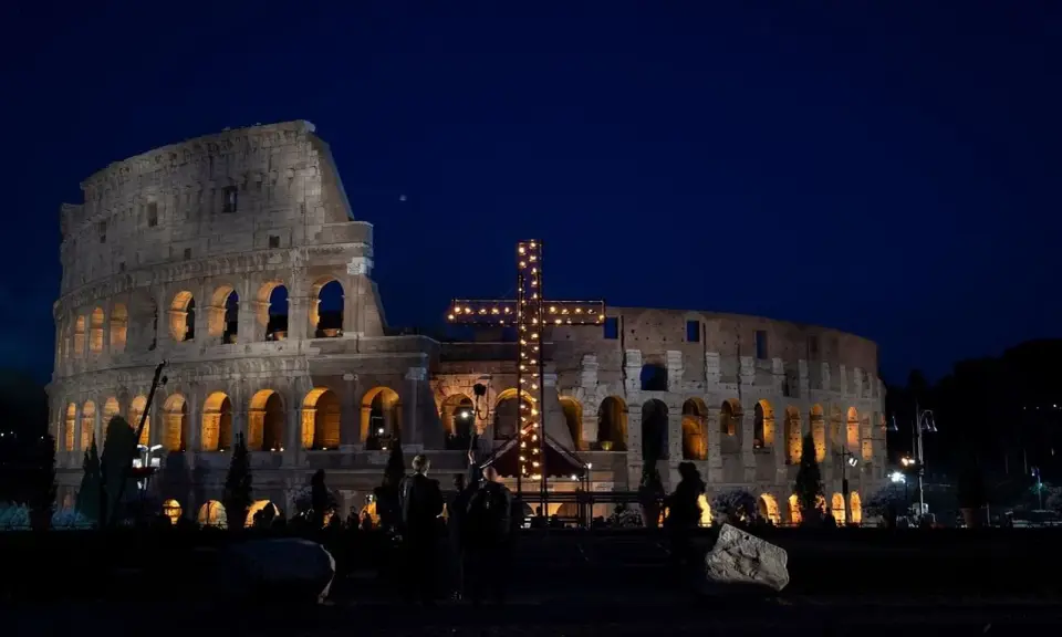 Colosseo illuminato di notte con una croce luminosa, un'atmosfera suggestiva che ricorda quando si festeggia Pasqua.