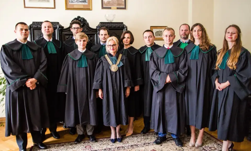 Grupa prawników w togach stoi w pomieszczeniu.