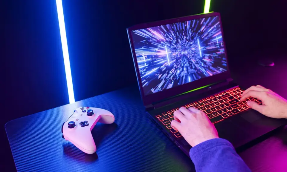 Un joueur utilise un PC portable gamer avec un clavier rétroéclairé. Une manette est posée à côté. Comment choisir son PC portable gamer ?