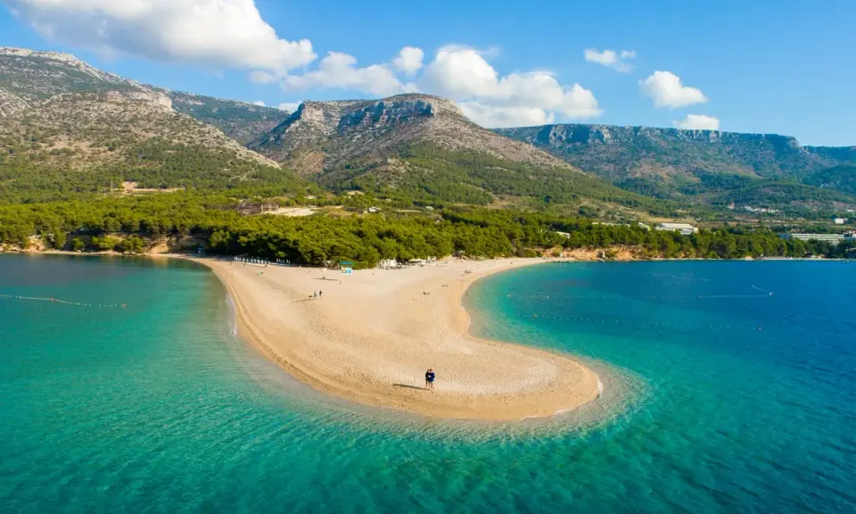 Spiaggia a forma di lingua di sabbia dorata, bagnata da acque cristalline, con montagne verdi sullo sfondo. Un angolo di paradiso in **Croazia mare**.