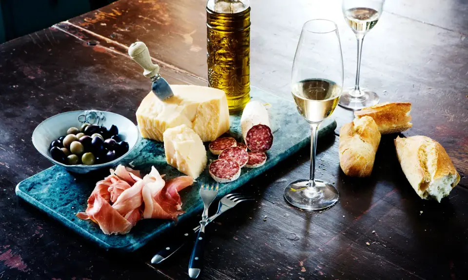 En härlig italiensk buffé med ost, salami, prosciutto, oliver, bröd och ett glas vitt vin, kanske en riesling druva.