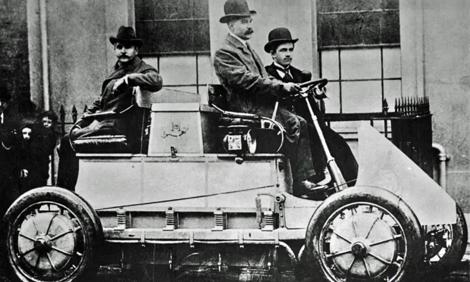 Hombres con sombreros posan en el primer coche eléctrico de la historia, un vehículo pionero de finales del siglo XIX.