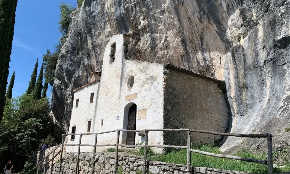 Piccolo eremo di San Valentino incastonato nella roccia, con un campanile a vela e un sentiero che conduce al suo ingresso.