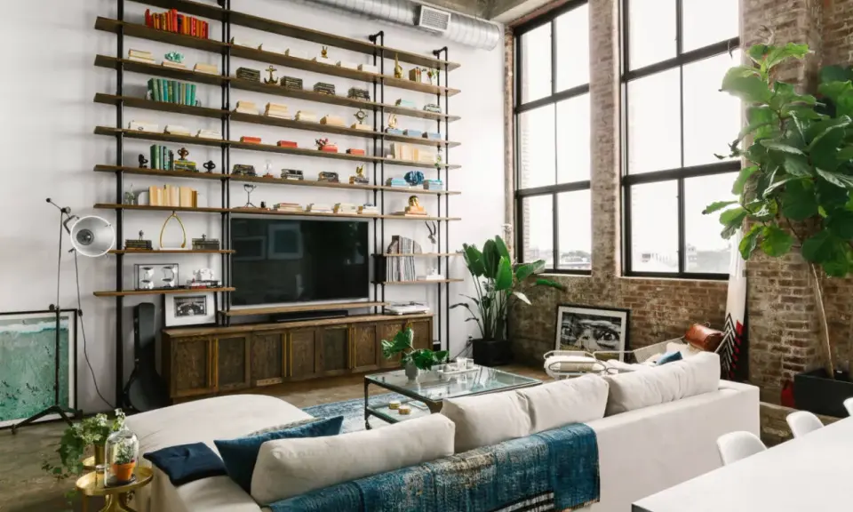 Soggiorno con scaffalatura a tutta parete, TV e divano bianco. Il soffitto alto 5 metri crea un'atmosfera ariosa, accentuata dalle grandi finestre.