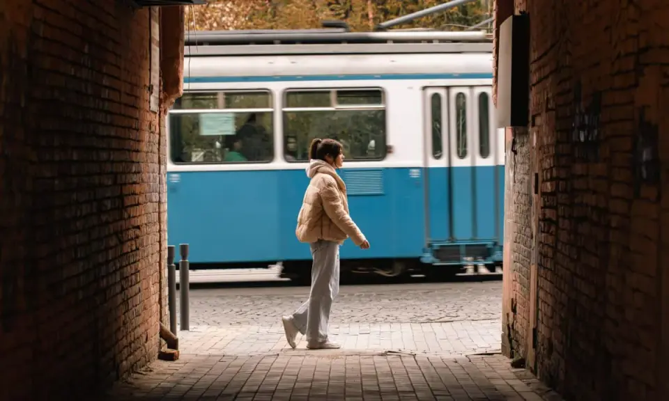Una ragazza cammina in un vicolo, un tram blu sfreccia sullo sfondo. Una foto vedo non vedo che cattura un momento fugace.