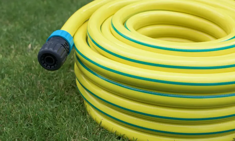 Un tuyau d'arrosage jaune enroulé sur l'herbe, avec un connecteur noir et bleu. Le diamètre du tuyau d'arrosage est visible dans son enroulement.