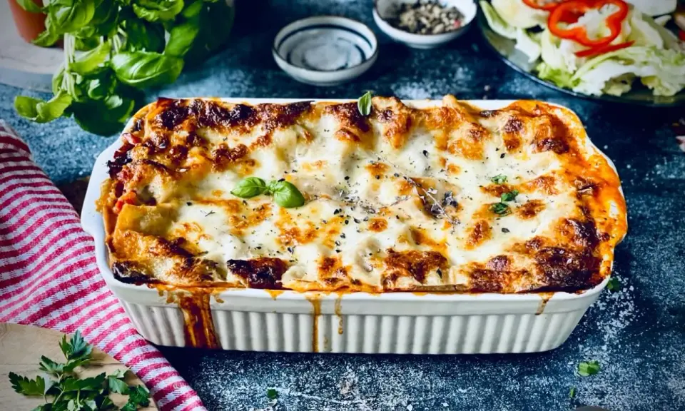 Herzhafte vegetarische Lasagne mit geschmolzenem Käse und frischem Basilikum, serviert in einer weißen Auflaufform.