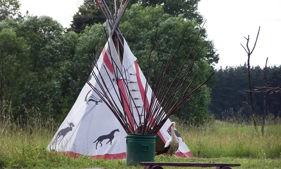 Wioska indiańska na Mazurach z tipi ozdobionym zwierzętami, bocianem i łukami.