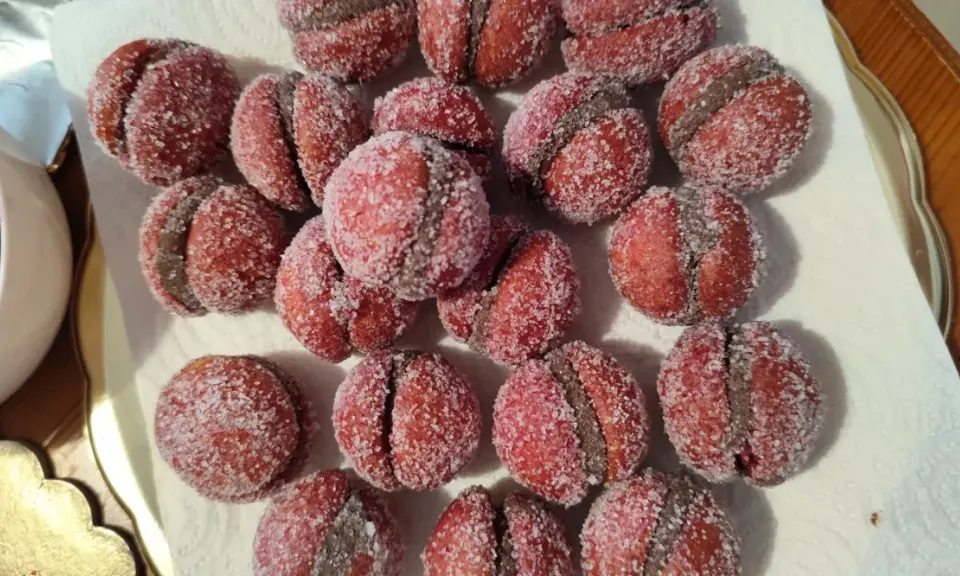 Dolci castagnole romagnole, due semisfere rosse unite da una crema scura e ricoperte di zucchero.