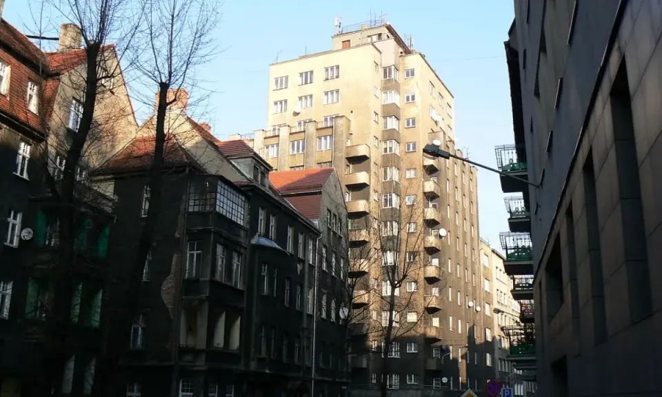 Wysoki, jasny drapacz chmur w Katowicach góruje nad starą kamienicą.