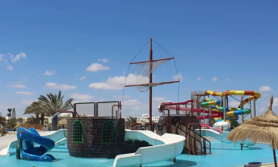 Djerba Aqua Resort (ex. Sun Connect) z pirackim statkiem i kolorowymi zjeżdżalniami wodnymi pod błękitnym niebem.