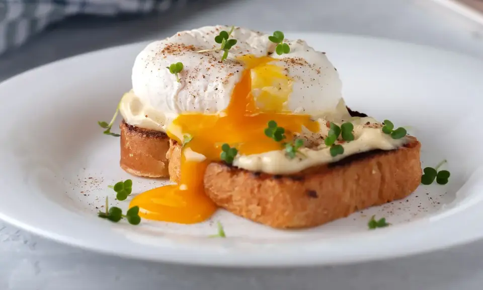 Un delicioso huevo poche con yema líquida cayendo sobre tostadas, adornado con brotes verdes y pimienta.